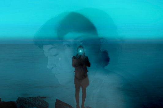 Moody double-exposure self-portrait photograph by Paige Griffin (HāPaige), showing a silhouetted figure standing by the ocean at dusk with layered faces and teal-blue tones, blending introspective portraiture with coastal landscape photography.