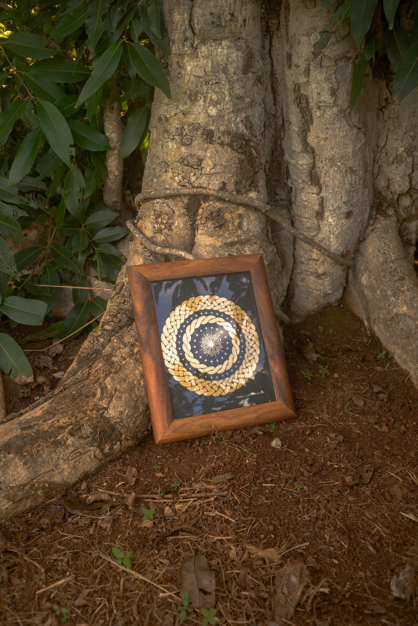 Shiny golden celtic braid painting with black background, leaning against tree trunk.