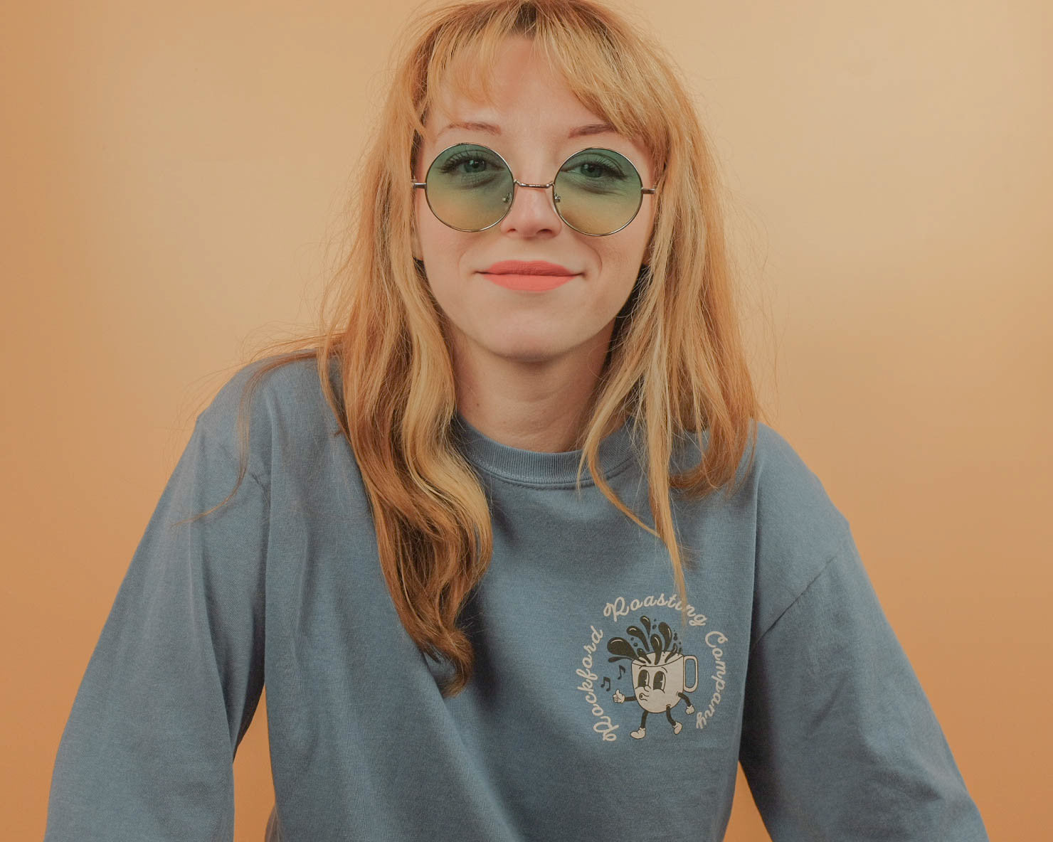 Person wearing a blue t-shirt with a logo against a beige background