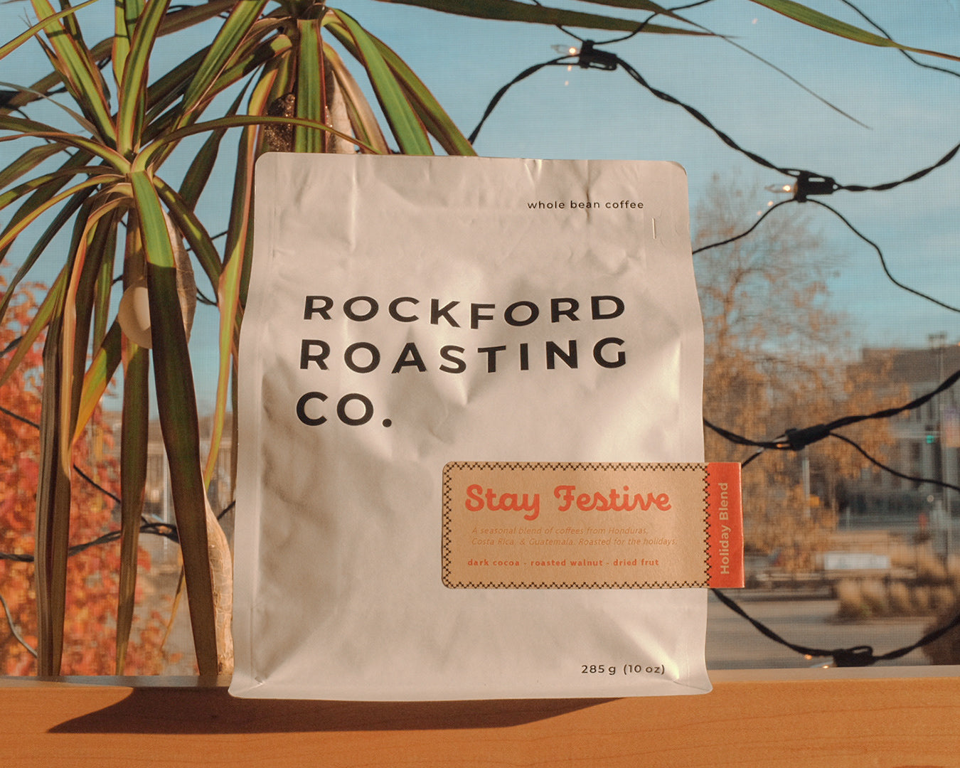 Rockford Roasting Co. coffee bag with 'Stay Festive' label on a wooden surface with plants in the background