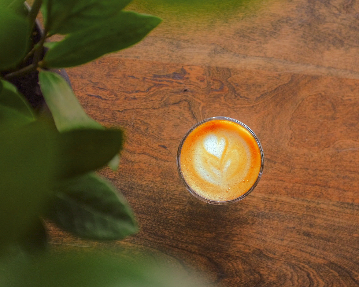 Cortado in a glass on a wooden table with a plant in the corner